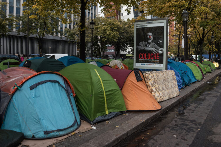 Des tentes Quechua dans lesquelles survivent des personnes migrantes, à Paris en 2016, déployées autour d'un panneau publicitaire faisant la communication de l'exposition "Coluche"... © Frédéric Legrand - Shutterstock