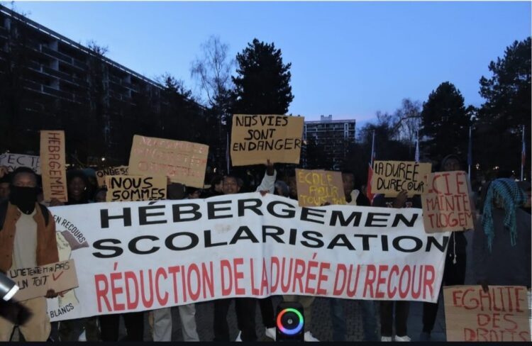 Les jeunes tenant des pancartes "Une tente n'est pas un toit" ; "Nos vies sont en danger", ainsi qu'une banderole reprenant les trois mots d'ordre de leurs revendications : un hébergement digne, une scolarisation immédiate et la réduction de la durée du recours. © Katy M. / Lisbeth